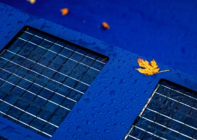 Panneau solaire bleu avec gouttes d'eau et feuille jaune posée dessus, sur fond bleu.