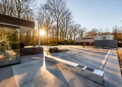 Maison moderne avec terrasse en béton, arbres dénudés et soleil couchant à l'arrière-plan, reflet d'un sapin décoré dans une vitre.
