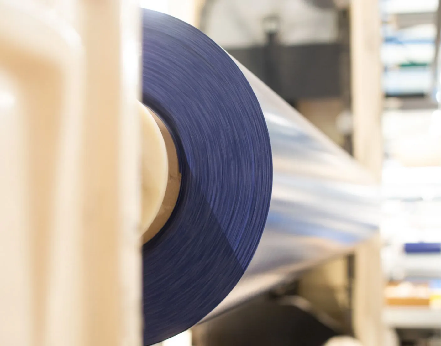 Rouleau de film plastique bleu enroulé sur une machine industrielle dans un environnement de production clair.