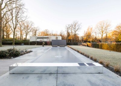 Une piscine couverte d'un volet miroir est entourée d'un jardin avec des arbres dénudés et une pelouse givrée.