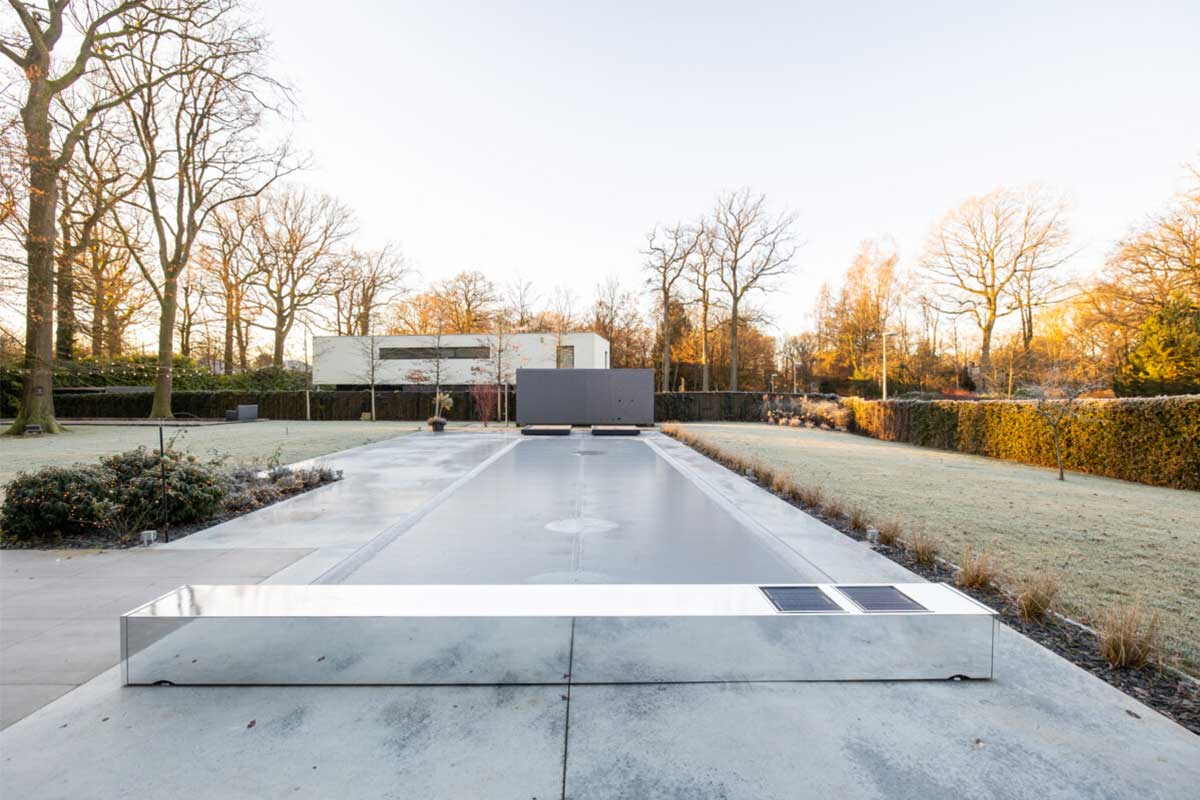 Une piscine couverte d'un volet miroir est entourée d'un jardin avec des arbres dénudés et une pelouse givrée.