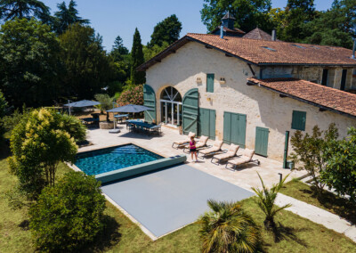 Vue aérienne d’une maison en pierre avec piscine équipée d’une couverture Coverseal grise, intégrée harmonieusement dans la terrasse en pierre claire.
